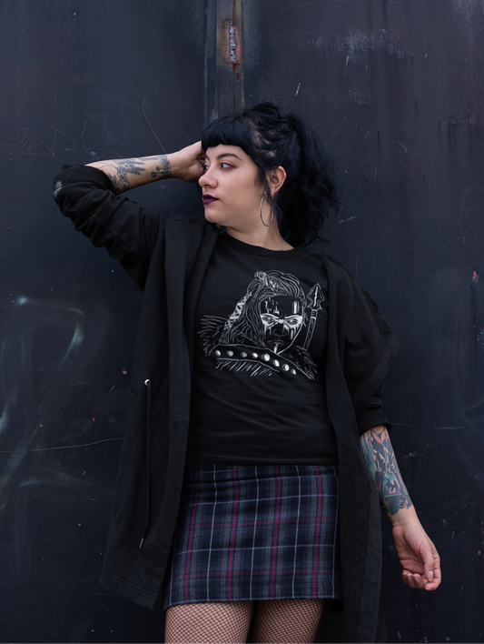Person wearing a black graphic t-shirt and plaid skirt against a dark wall